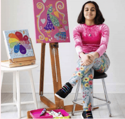 A girl sits on a stool next to a painting easel.