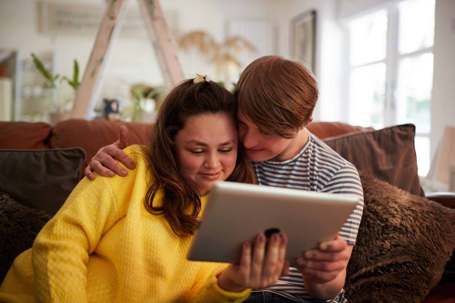 A man and woman are sitting on a couch looking at a tablet.