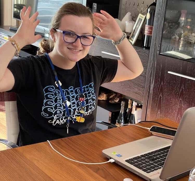 A girl with glasses is sitting at a table with a laptop.