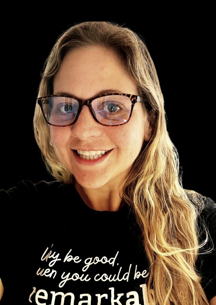 A woman in glasses wearing a t shirt that says if you be good you could be remakkal.