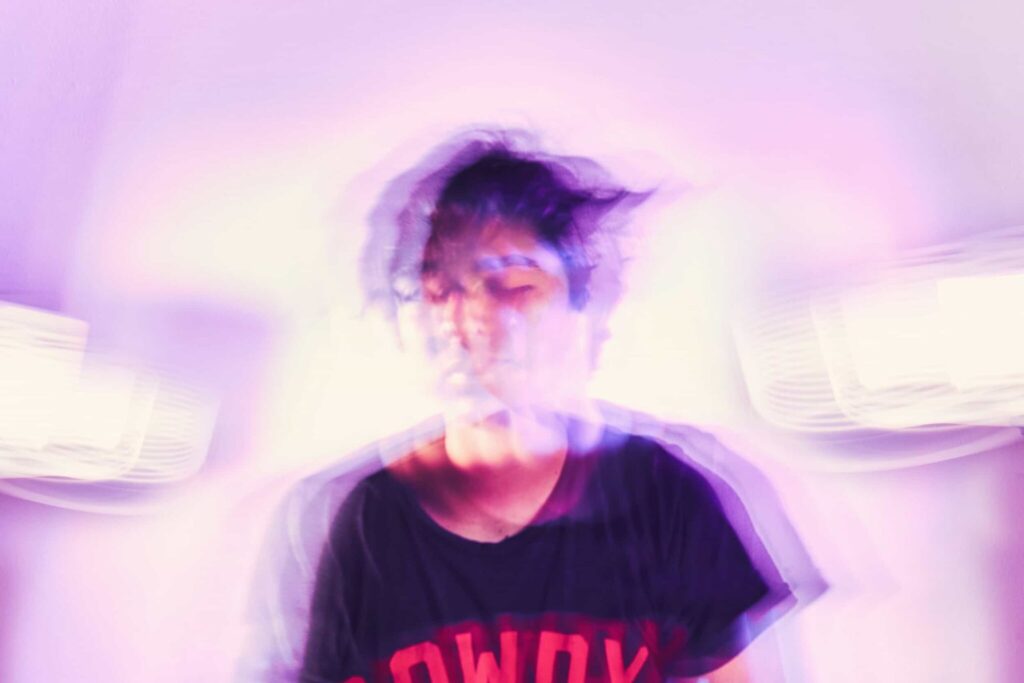A person wearing a dark t-shirt with red lettering is photographed with a blurred, double exposure effect against a light purple background, evoking the feeling of duality in functioning.